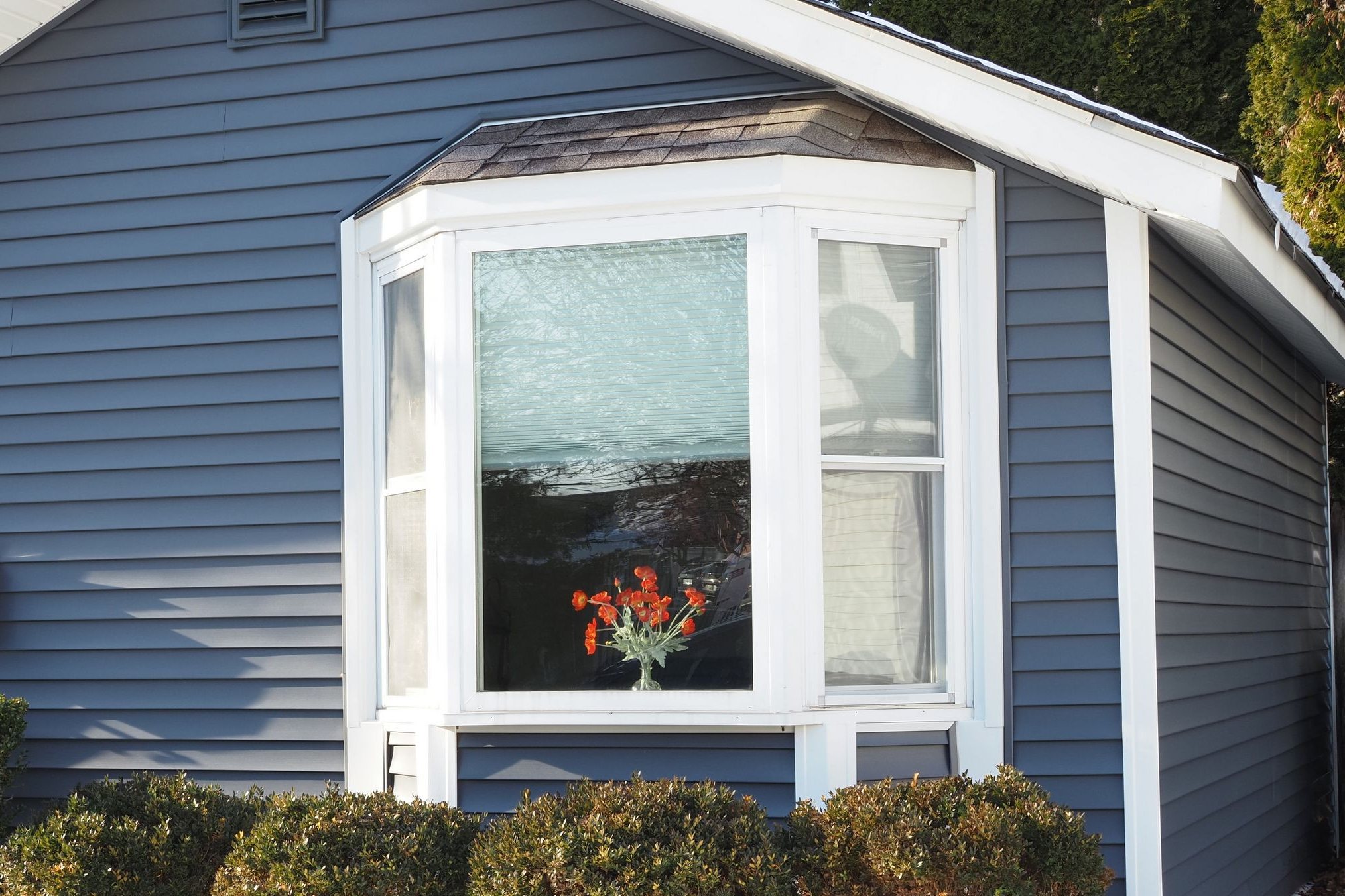 White bay window with three connected units under a shingled roof cap on blue siding