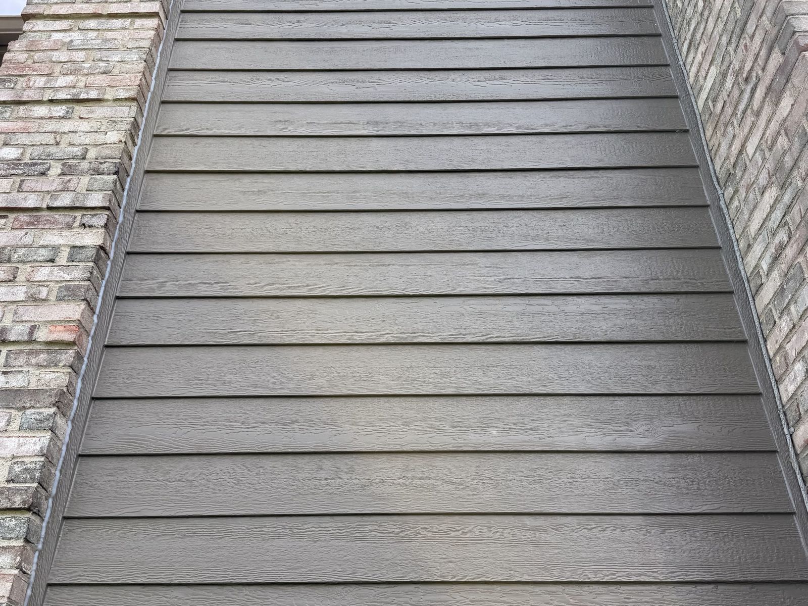 Brown lap Siding running up a narrow wall between two brick sections