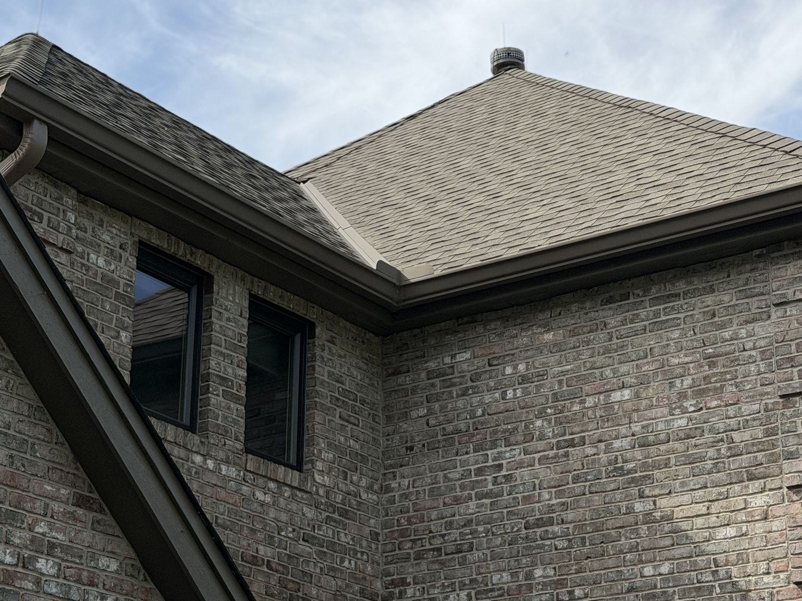 Shingled roof valley and Gutters above a brick two-story home with dark-framed Windows