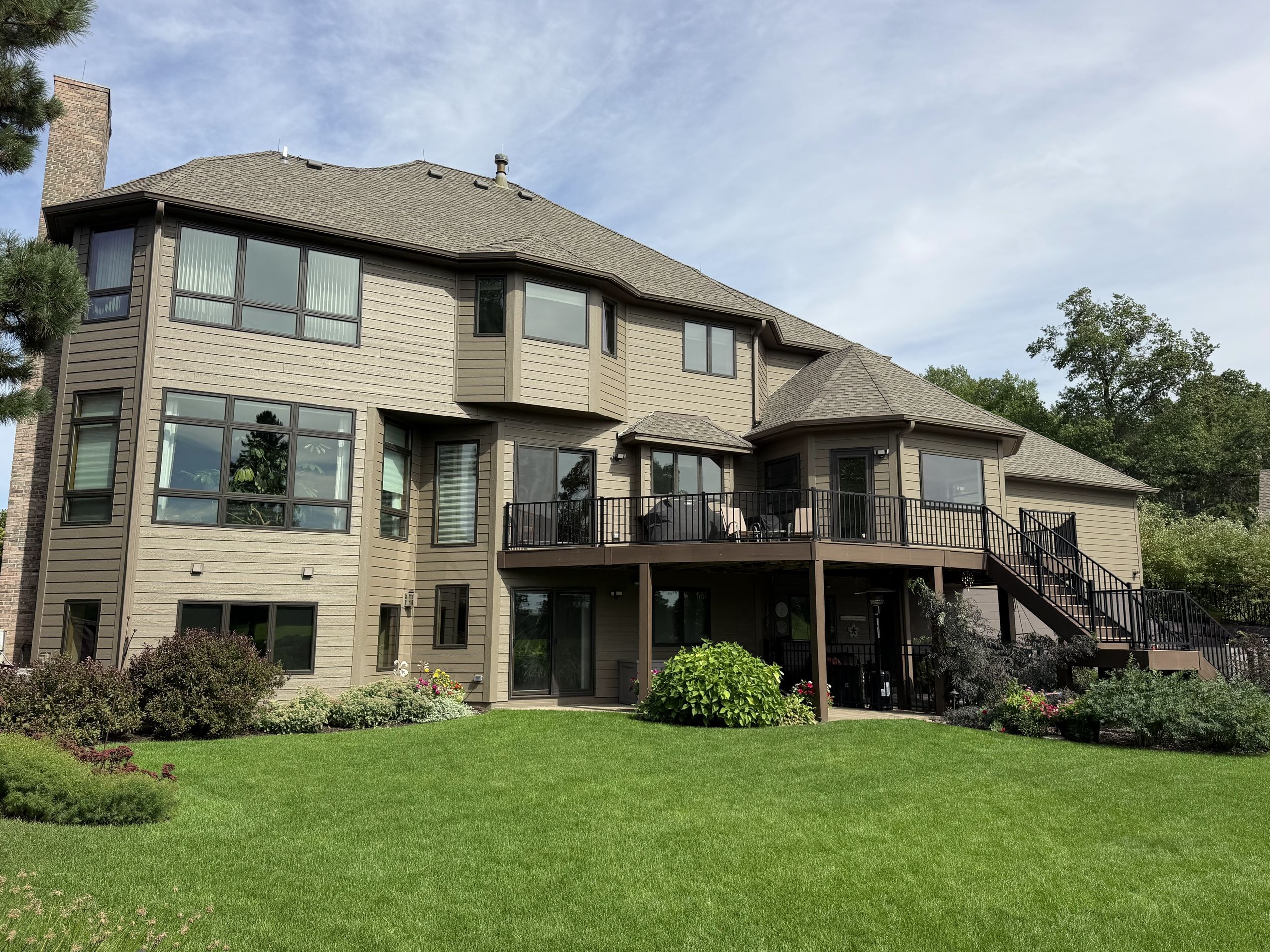 Rear elevation of a large two-story home with new tan lap Siding and Windows