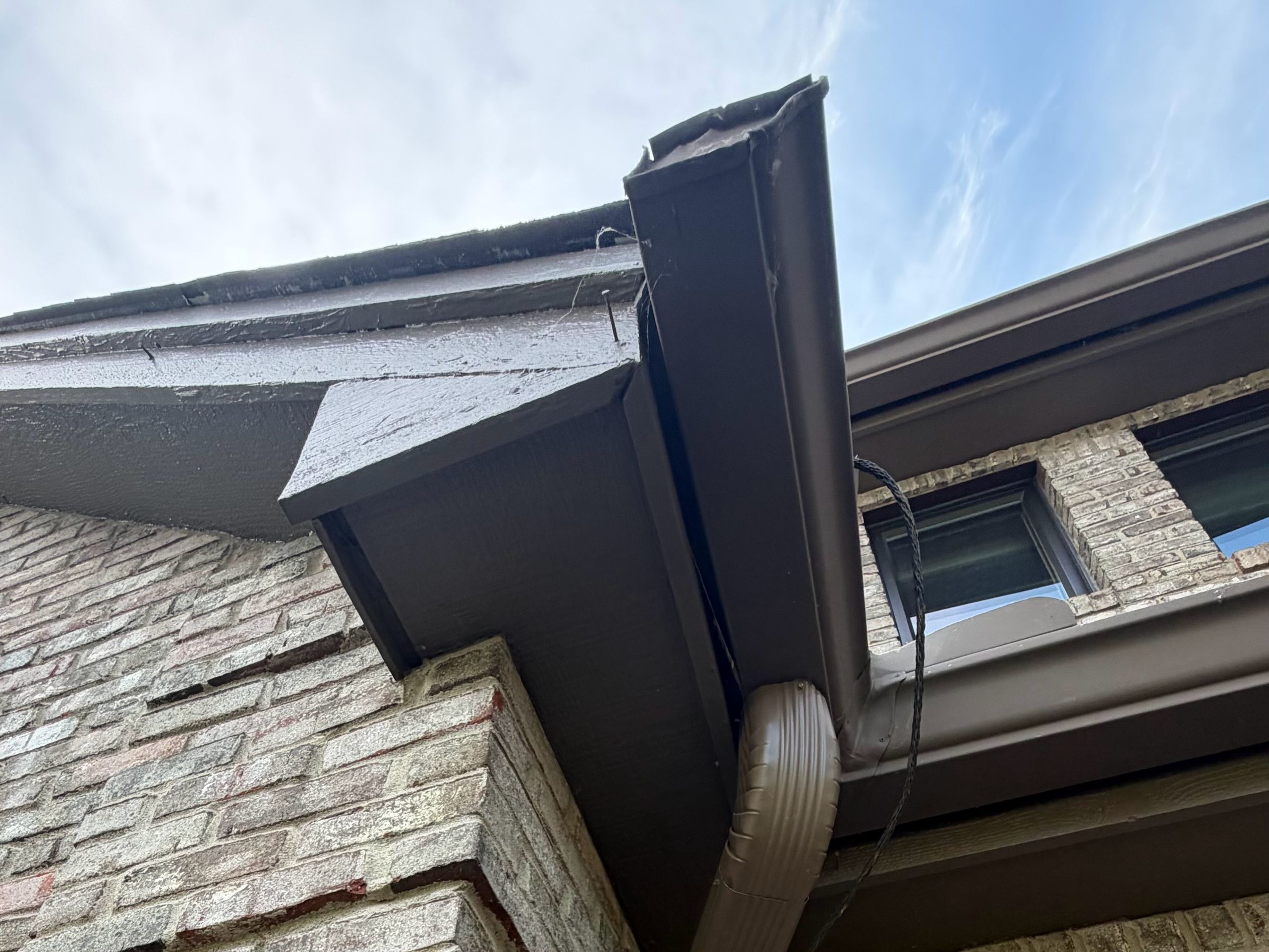 Gutter corner and downspout against the sky above a brick wall