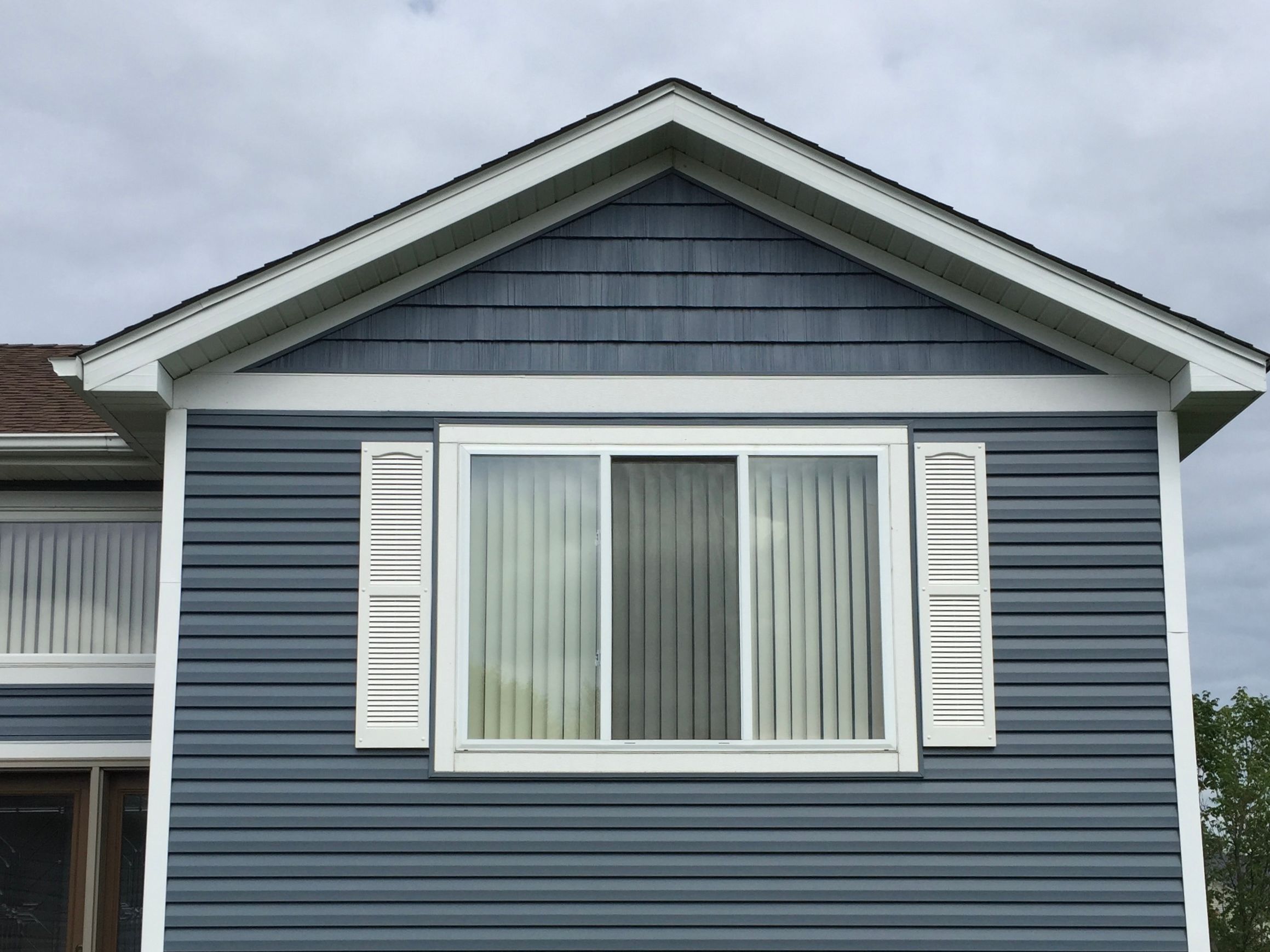 Blue vinyl lap Siding with a shake gable above a shuttered window