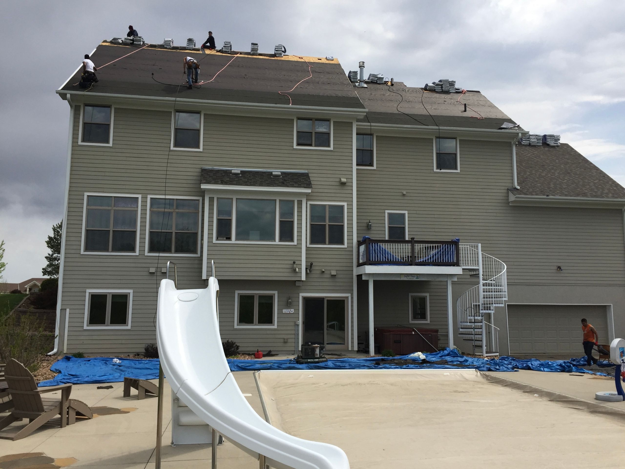 Crew re-roofing a three-story rear elevation above a pool deck