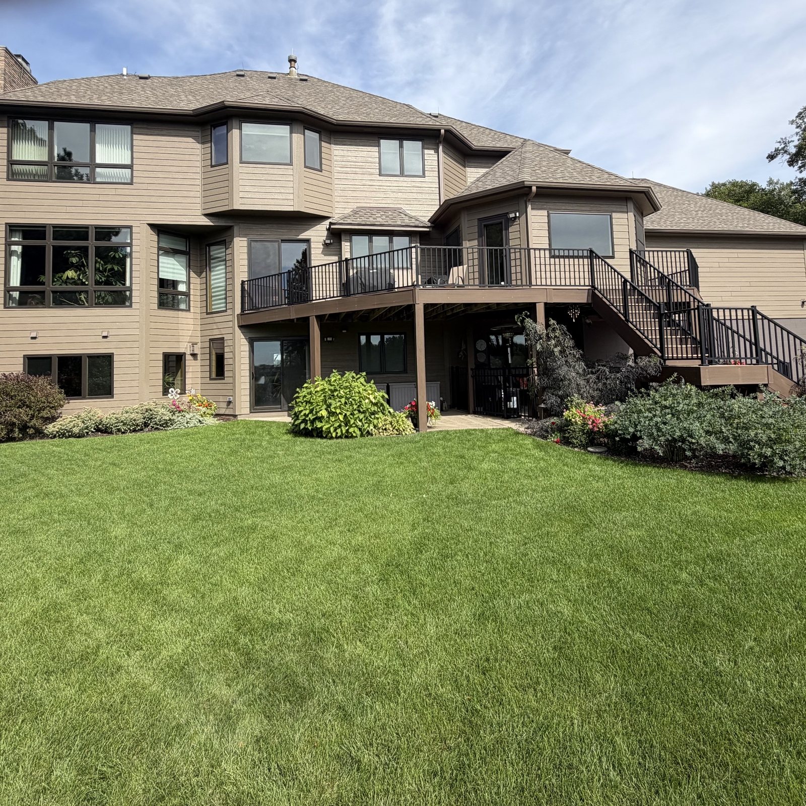 Wide lawn below the deck of a large tan-sided home