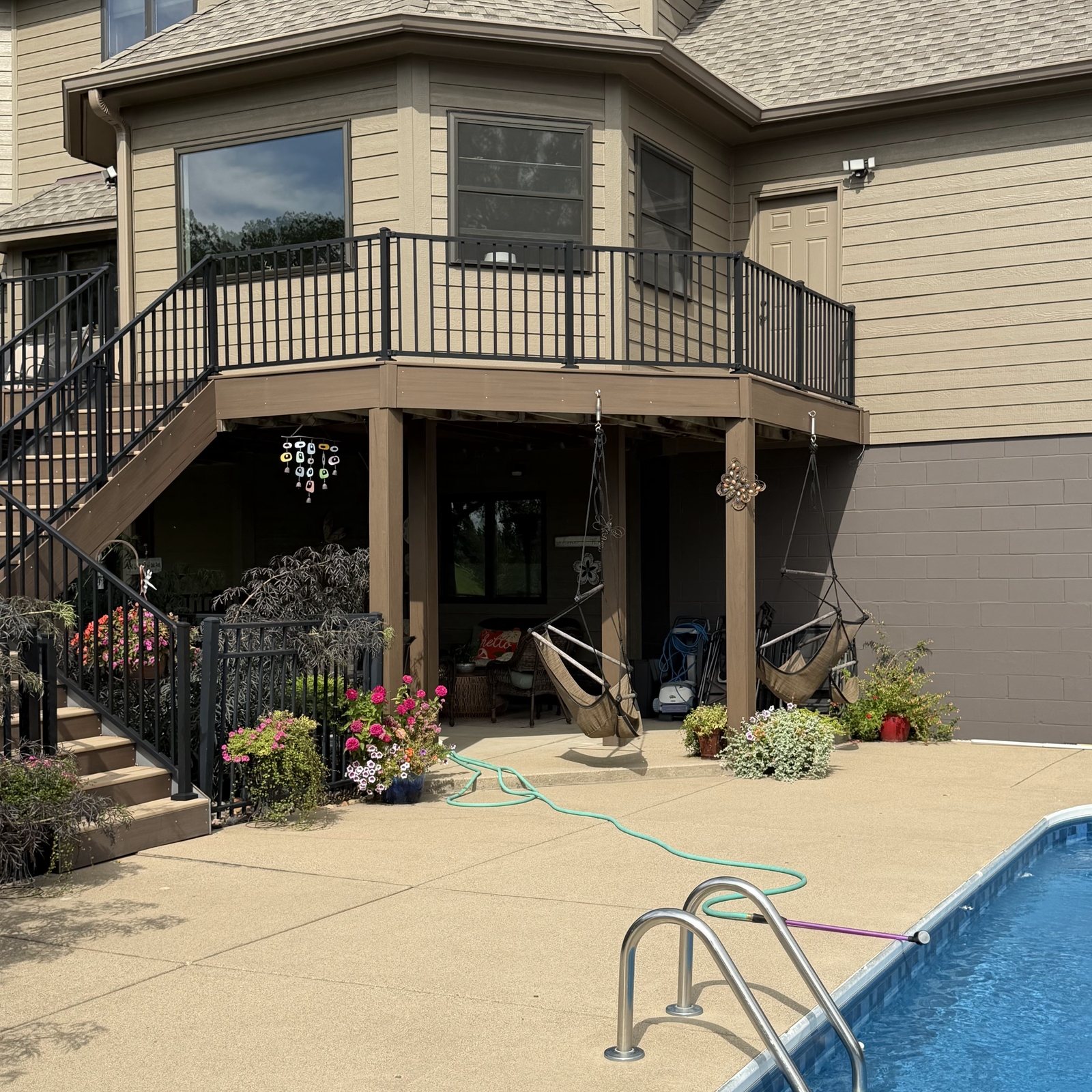 Pool steps and patio below a tan-sided bay and deck