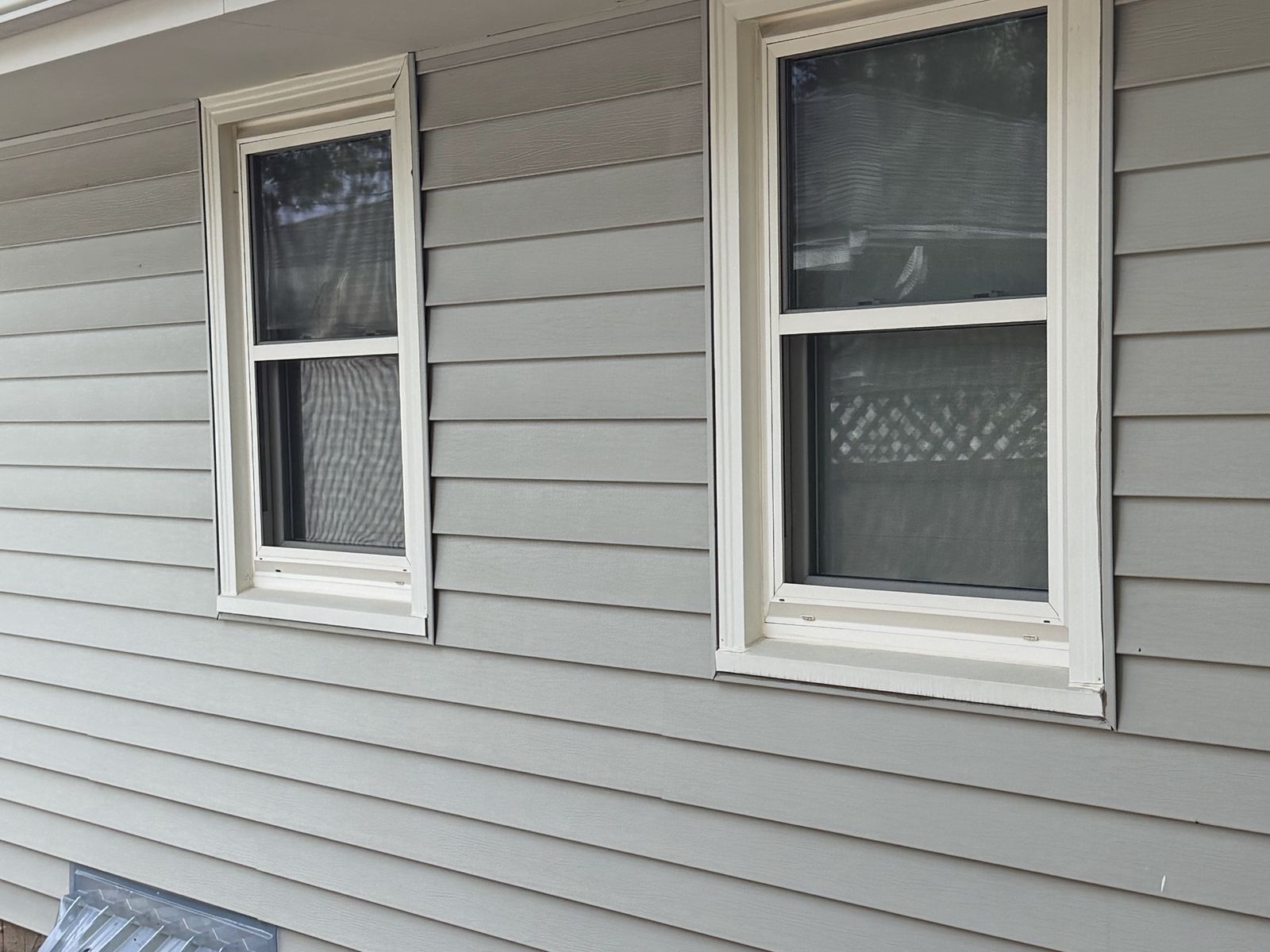 Two white Windows set in light gray lap Siding on the side of a rambler