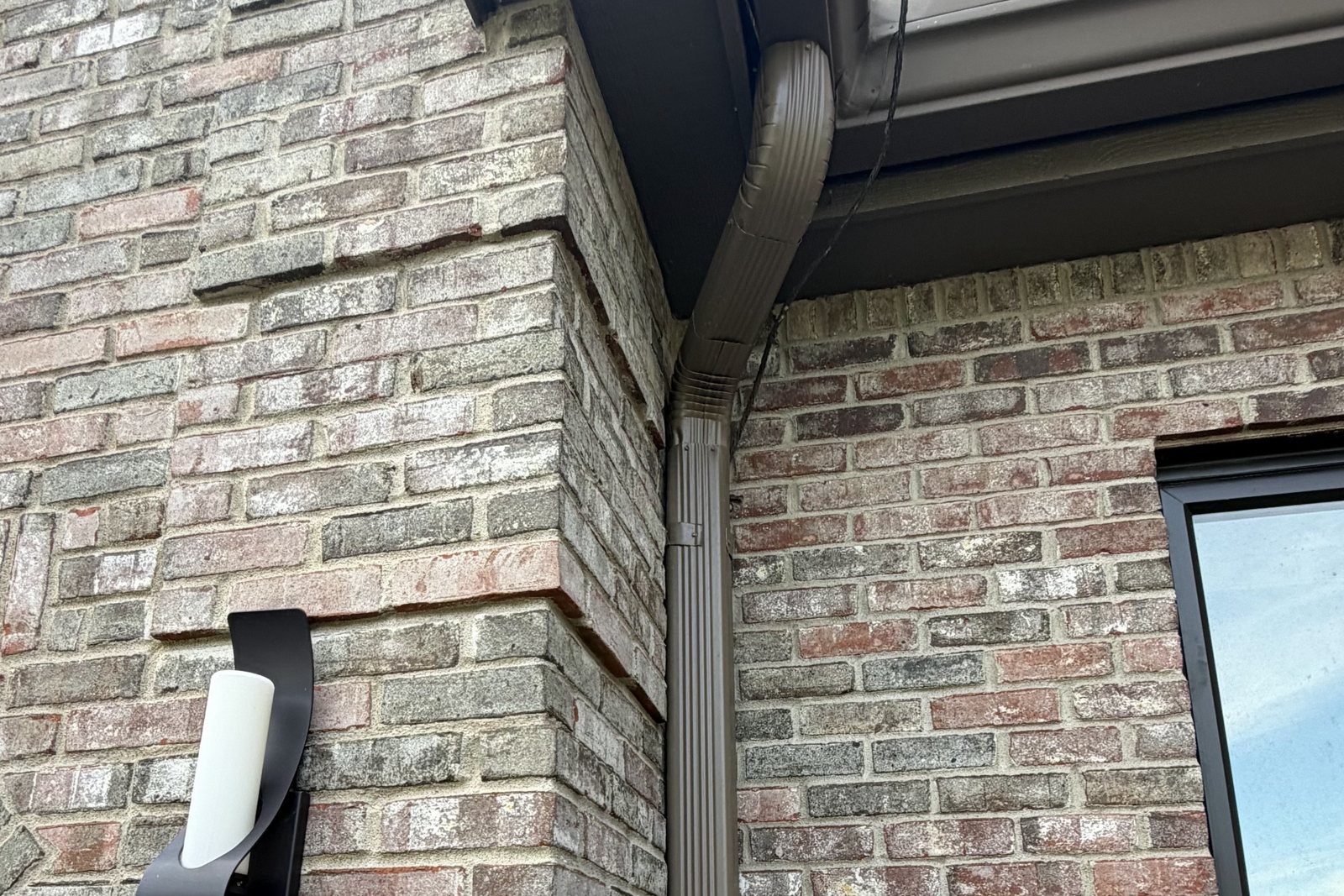 Downspout carried down a brick corner below new Gutters