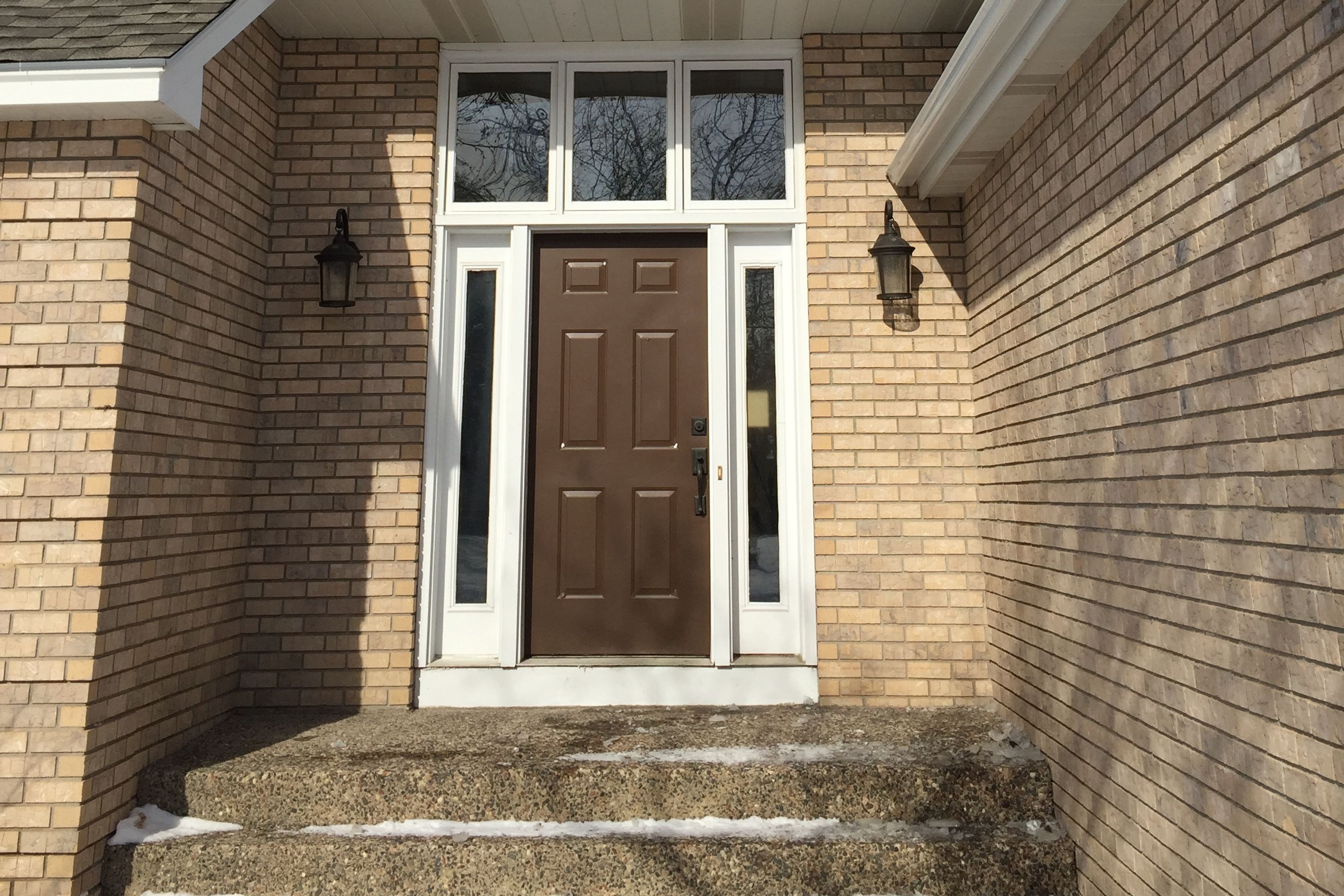 Brown entry door with sidelights and a transom in a brick entry