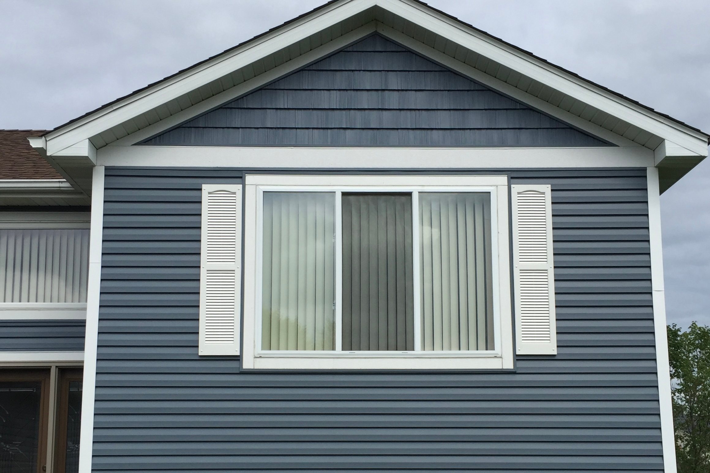 Blue-gray vinyl lap Siding with shake gable and white trim on a two-story home