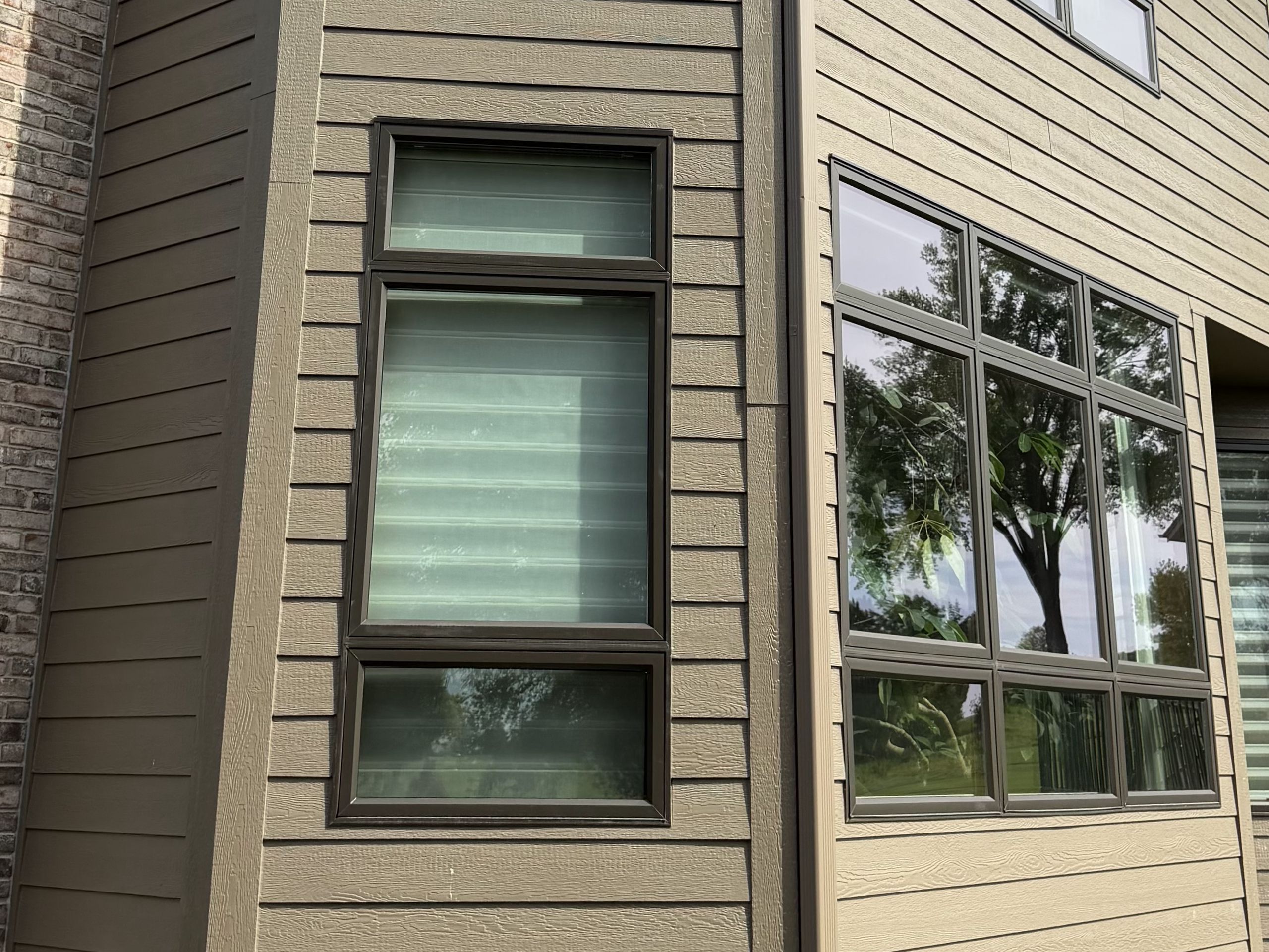 Corner of a tan-sided home with stacked replacement Windows