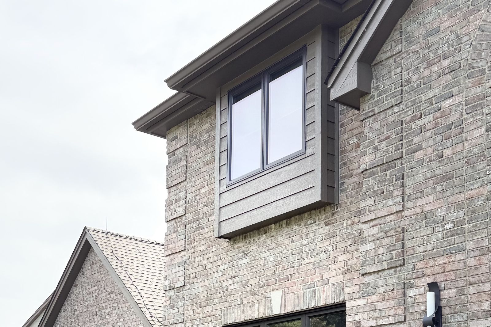 Upper-story window in a sided bay above a brick wall
