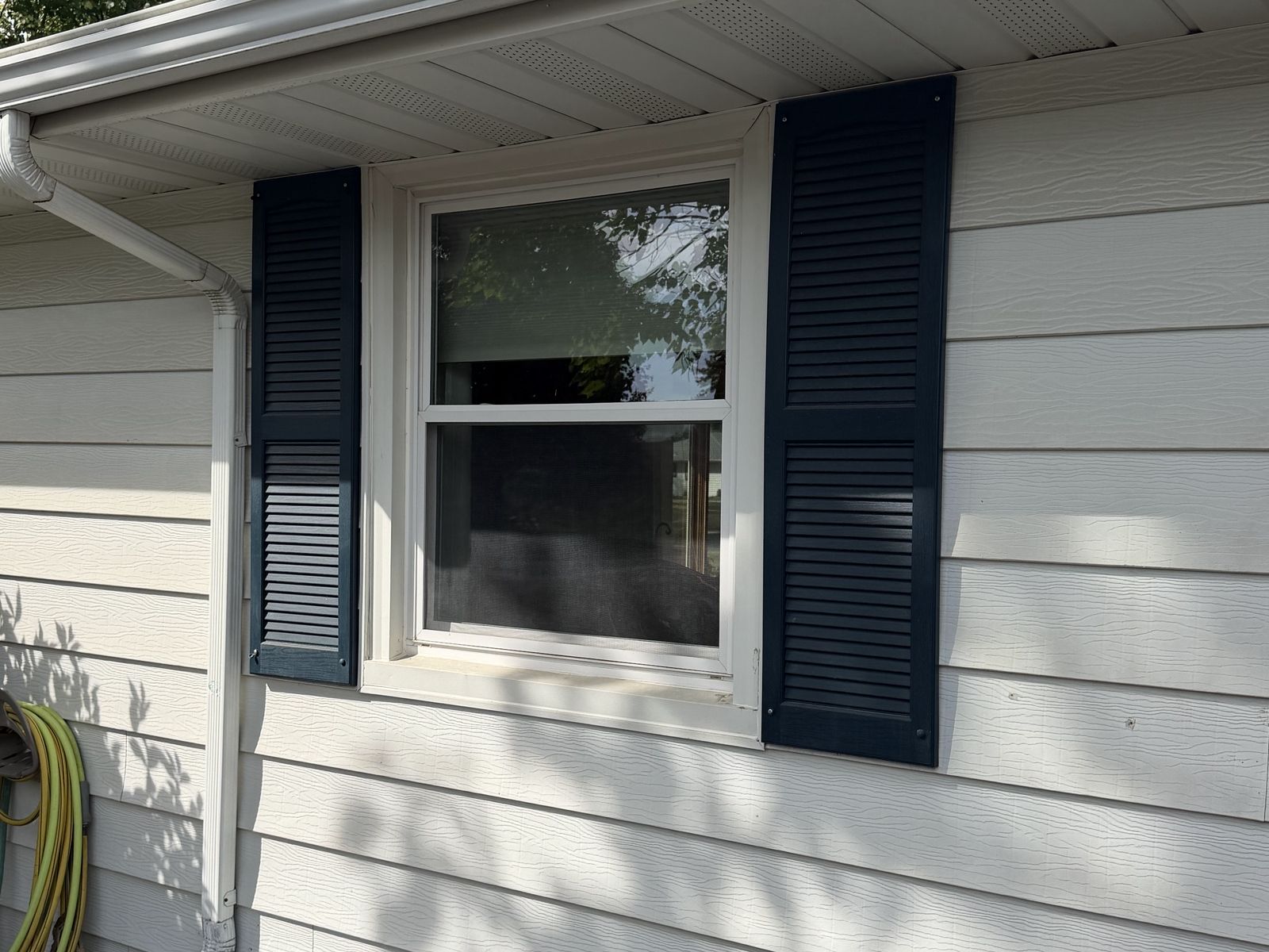 New window with black shutters centered in light lap Siding on a cream rambler